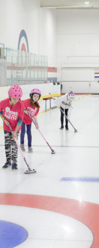 Three girls curling on the ice.