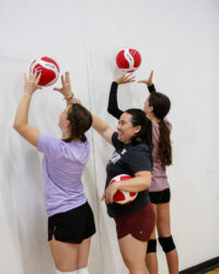2 girls with their coach practicing volleyball wall drills