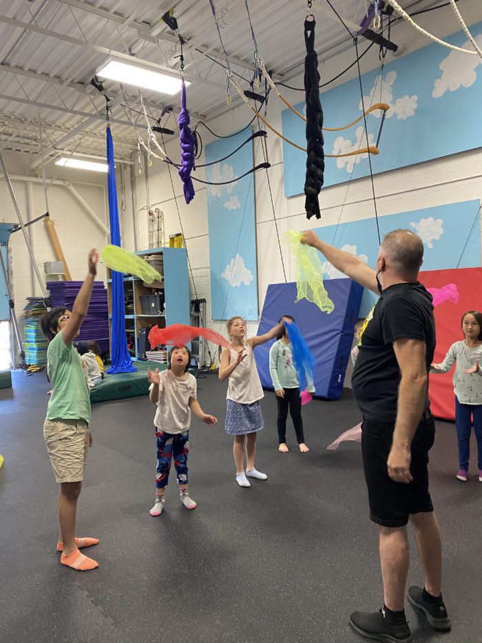 Group of girls learning to juggle scarves with male instructor.