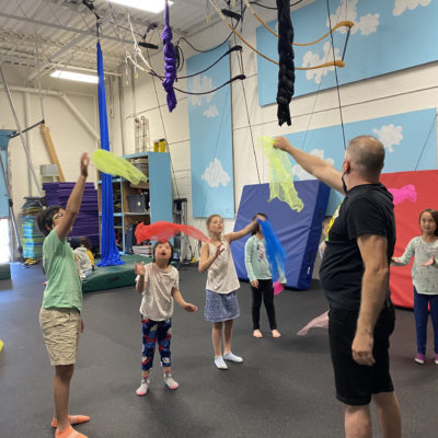 Group of girls learning to juggle scarves with male instructor.