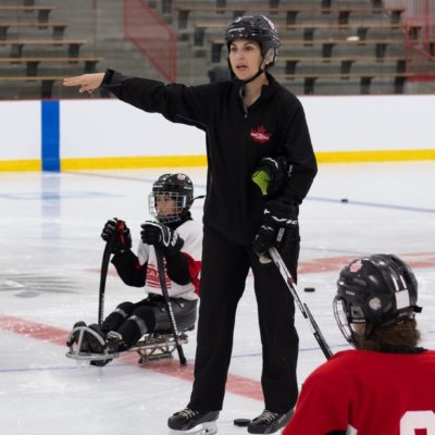 Female coach speaking to para ice hockey athletes on the ice