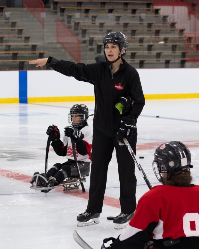 Female coach speaking to para ice hockey athletes on the ice