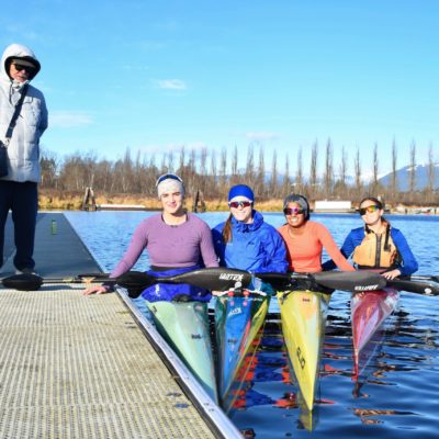 4 women in sprint canoes in the water beside a coach on the dock.