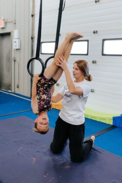 Girl being assisted by a coach on the rings