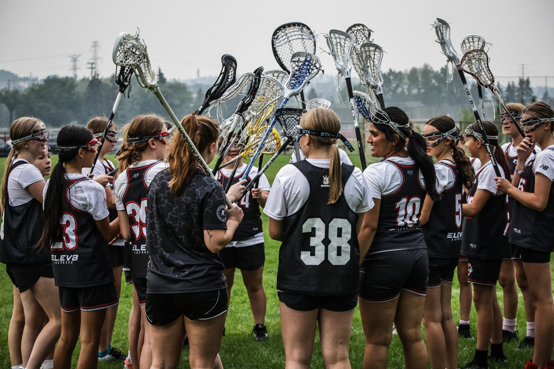 Group of girls in black jerseys raising their lacrosse sticks in a circle.