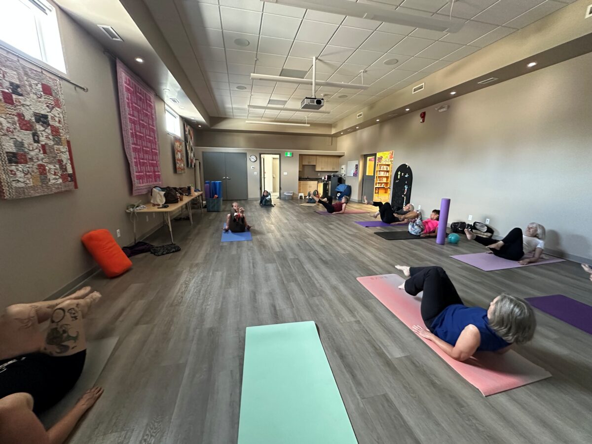 Group of women in an indoor studio doing yoga on mats.