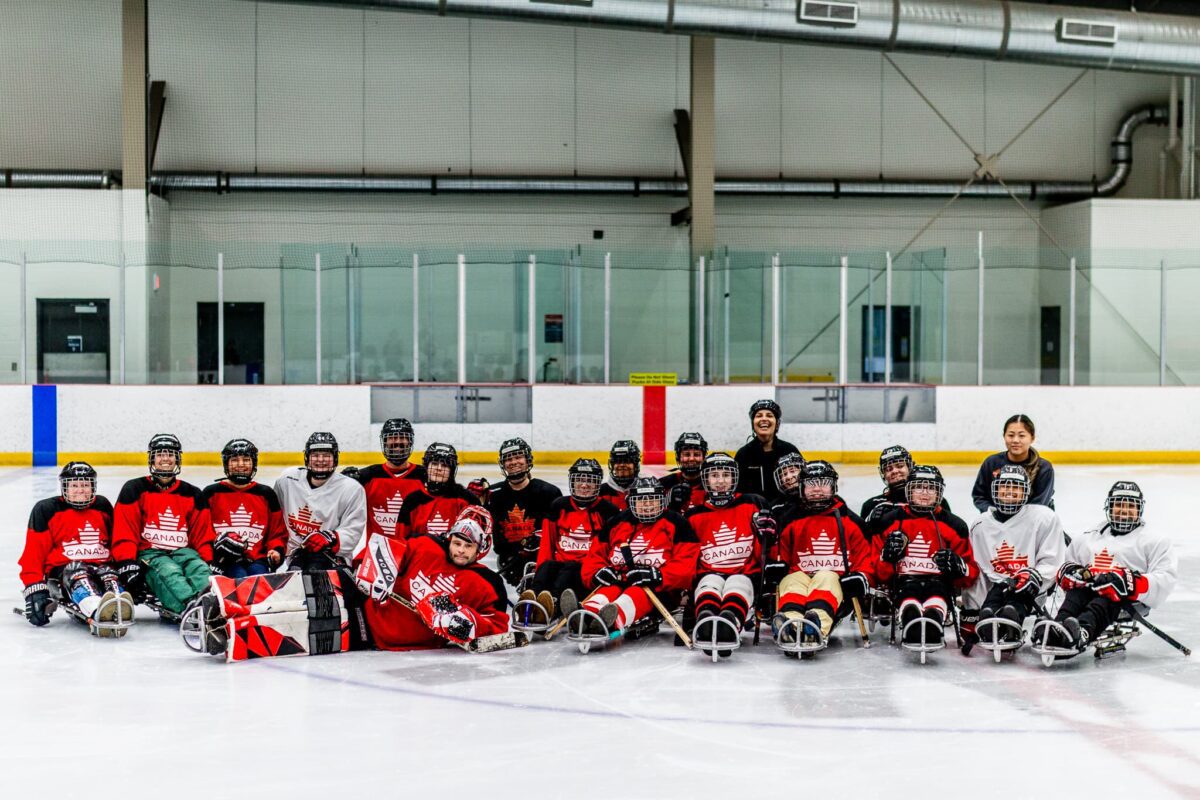 Group of para hockey players posing for a group phone on ice, in their uniforms and with their equipment.