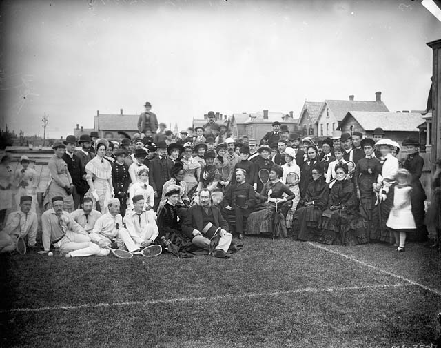 Historical photo of women and men with tennis racquets on an outdoor grass court.
