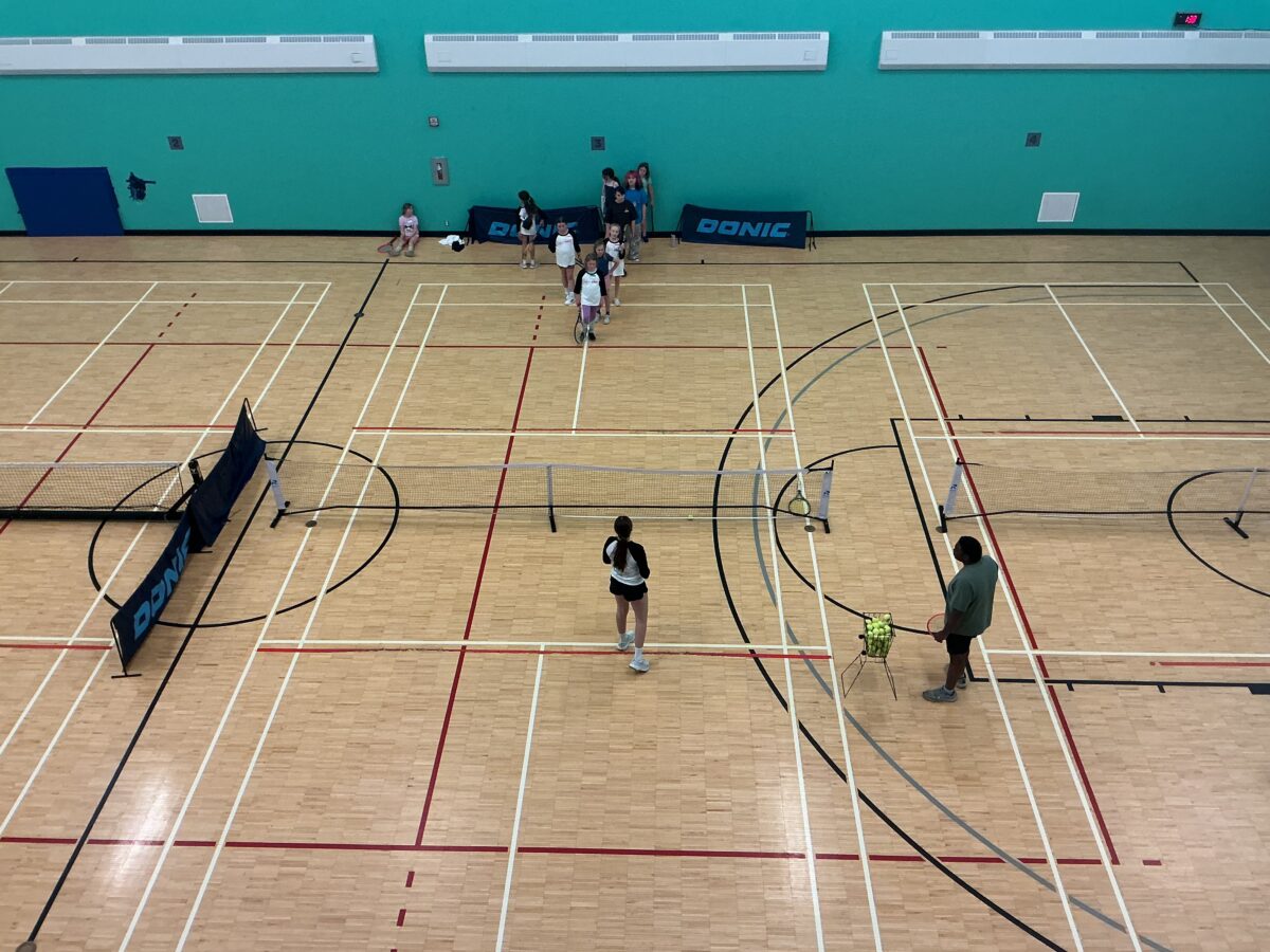 Overhead photo of a group of girls learning how to play tennis with a coach
