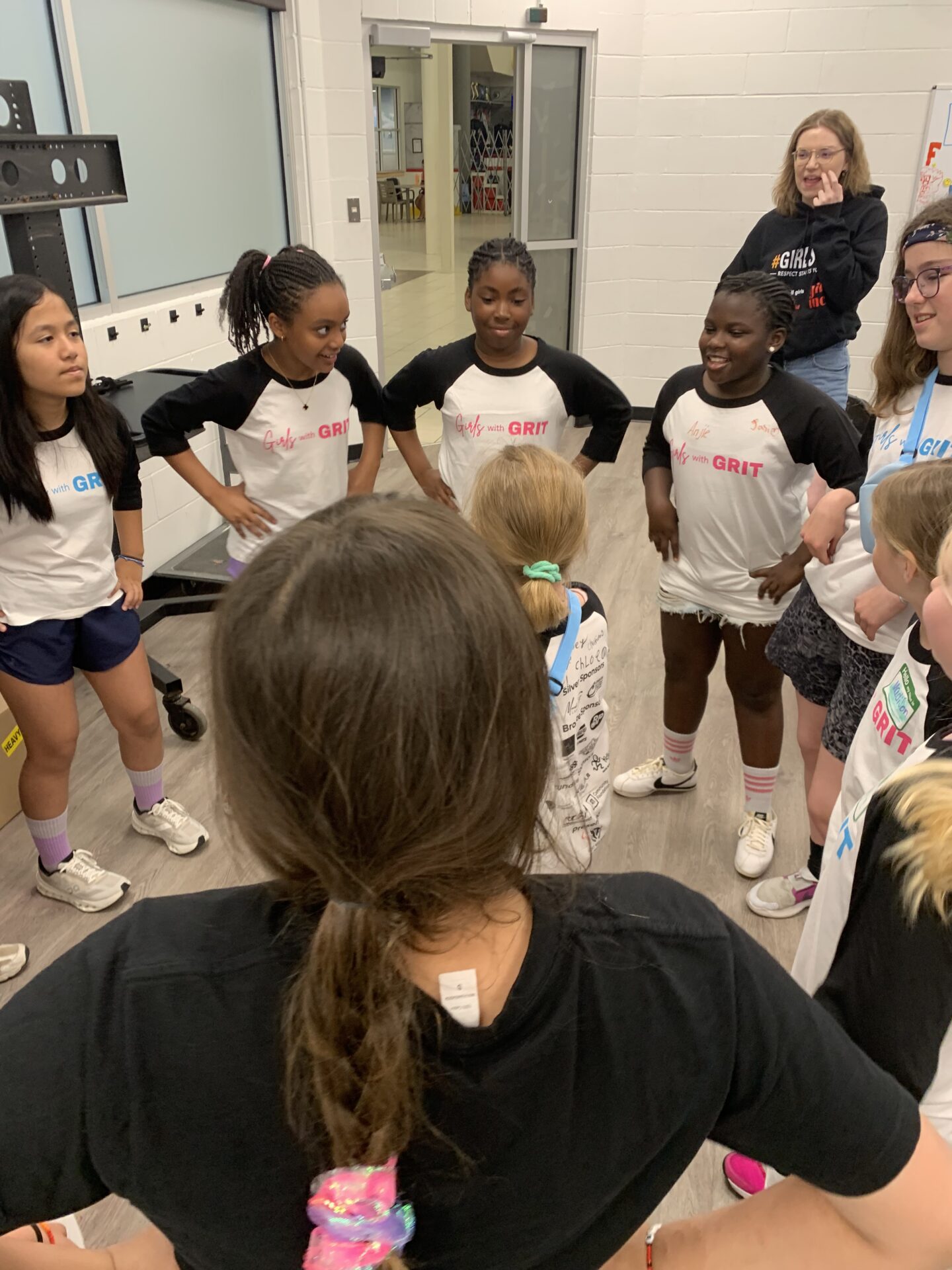 Group of girls in a circle listening to a coach in a gym.
