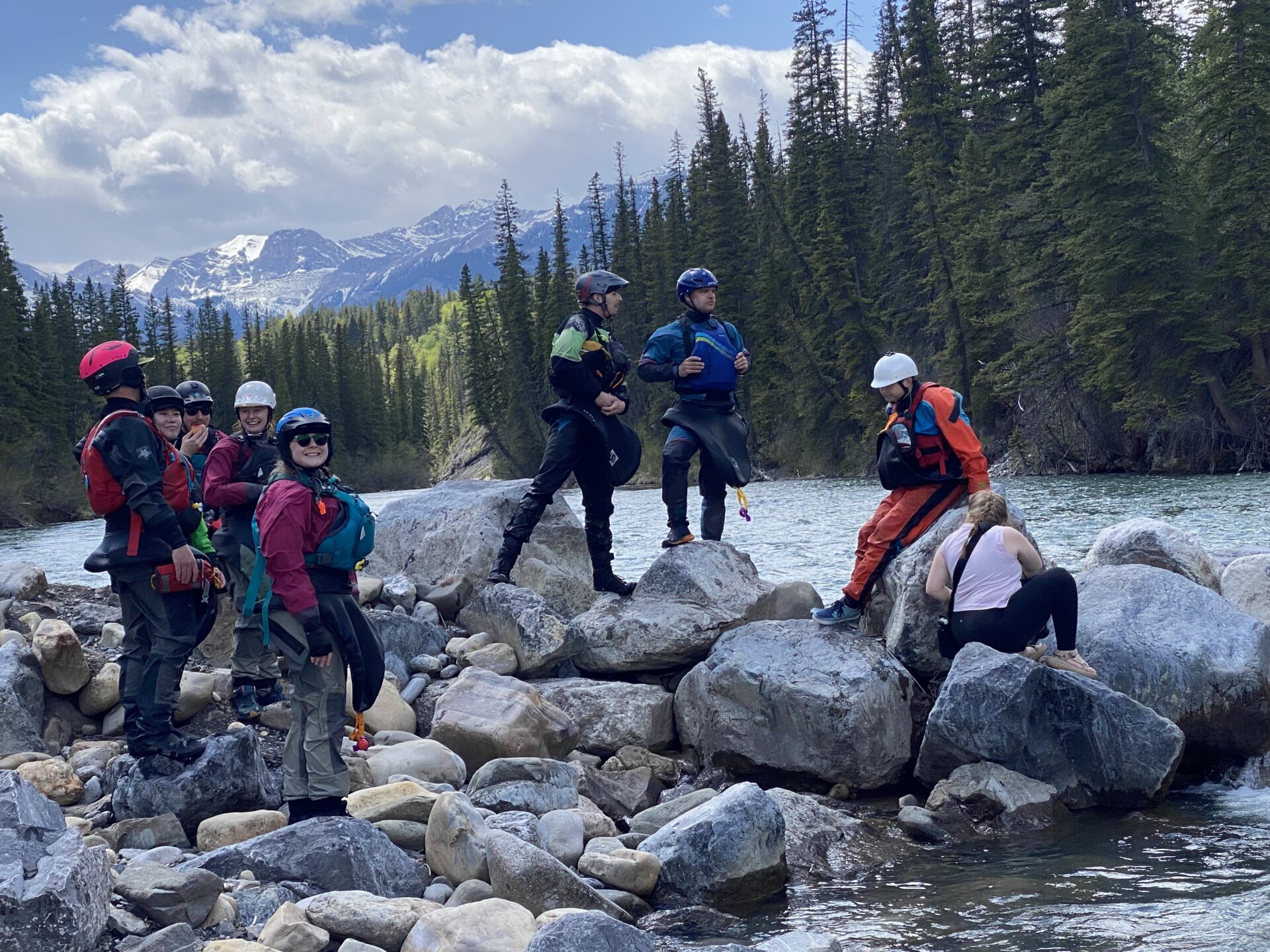Group of women in kayak gear standing on large rocks along a river.